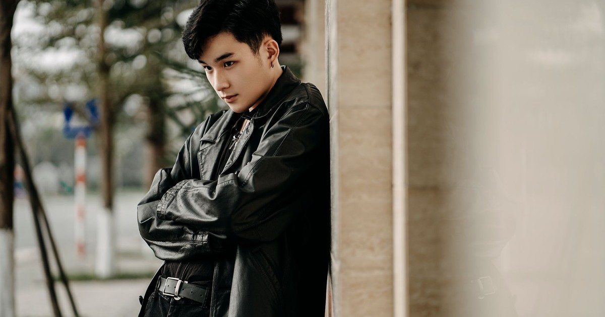 Self assured young Asian male in trendy black leather jacket standing with arms folded and looking away on street