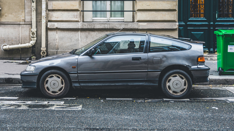 Gray Honda CR-X profile shot on city street in front of residential building