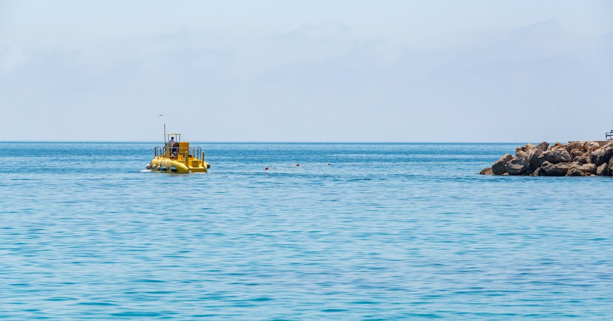 A yellow submarine navigates calm ocean waters against a clear sky near a rocky coastline.