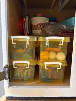 Stacked yellow storage boxes with toys inside on a shelf. Top shelf has various household items