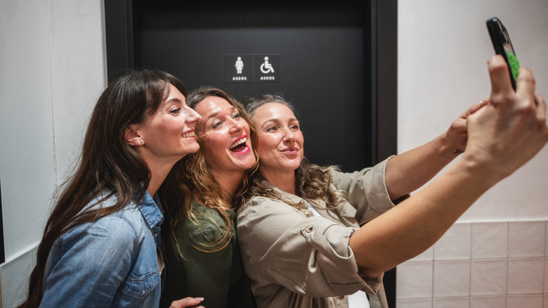 women taking a selfie in a public bathroom