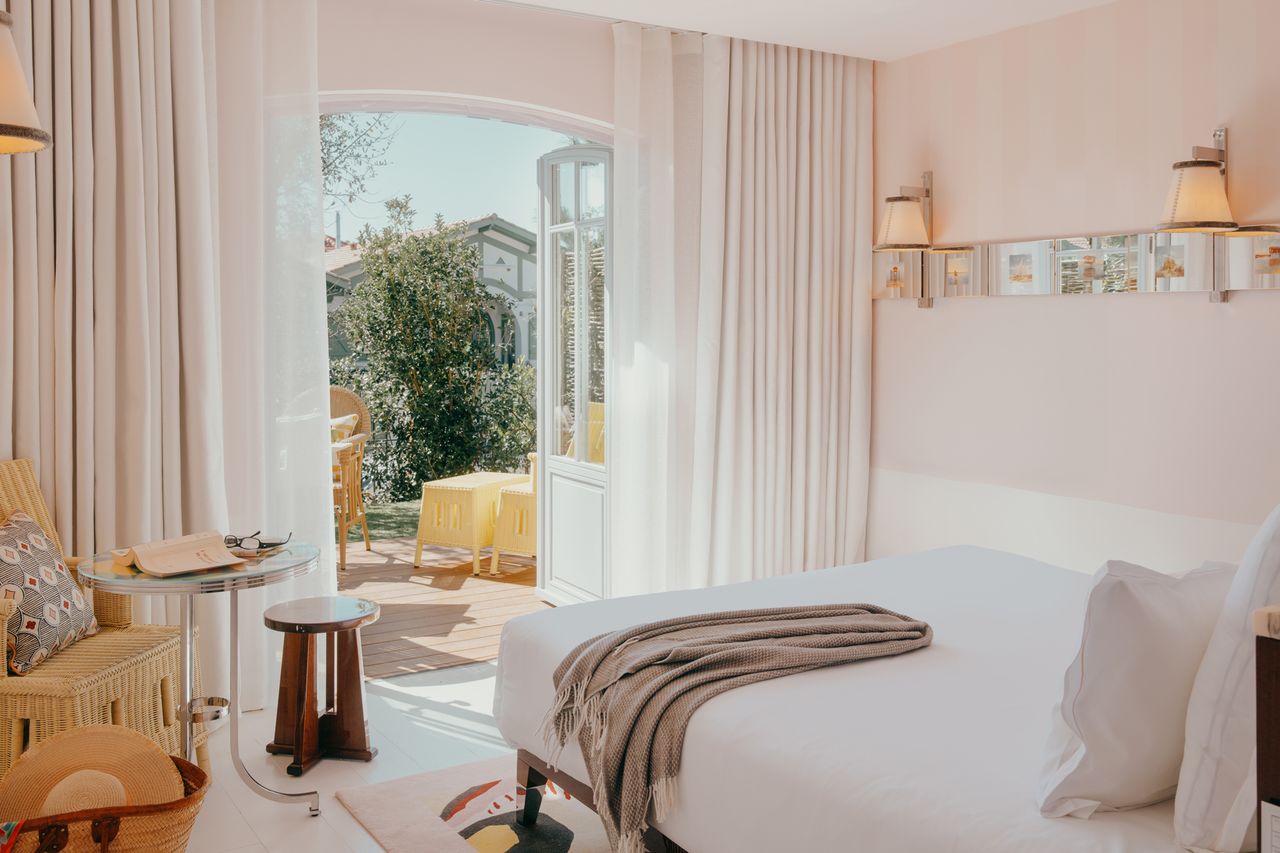 Welllit bedroom with a bed curtains and open doors leading to a patio with outdoor furniture