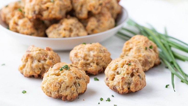 Sausage balls spilling from white bowl, next to bunch of fresh chives