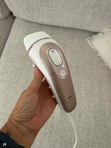 Hand holding a handheld hair removal device on a beige textured fabric background