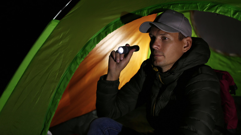 Man with flashlight sitting in tent at night