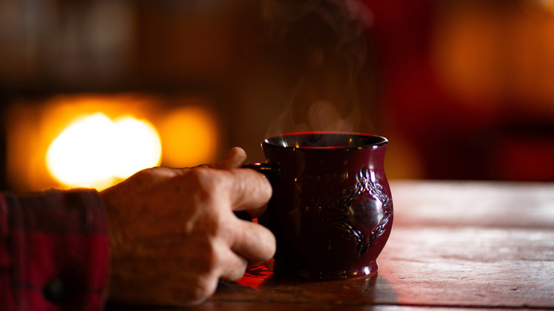 A hand holds a steaming cup of coffee on a saloon bar counter.