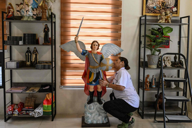 A woman cleans a statue of a saint displayed alongside books about exorcism at the Saint Michael Centre for Spiritual Liberation and Exorcism in Makati, Metro Manila. Photo: AFP
