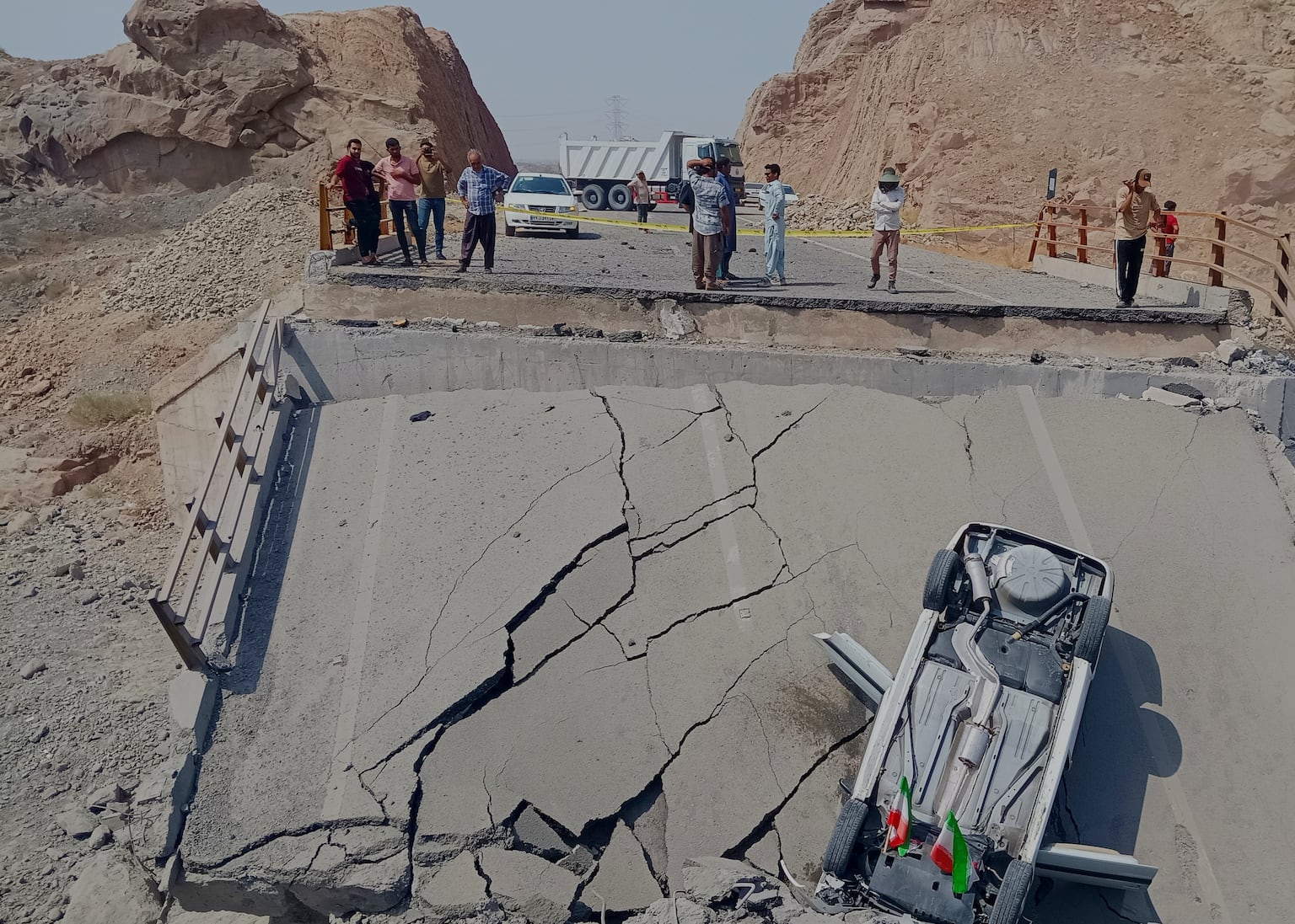An overturned car sits on a section of a destroyed bridge after a strike in Hormozgan province, southern Iran (Mahdi Negahban/Mehr News Agency via AP)