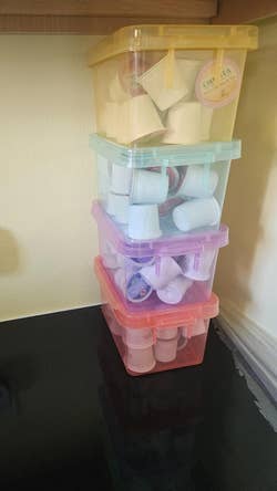 Stacked storage boxes filled with coffee pods on a kitchen counter near an outlet with a plugged-in air freshener