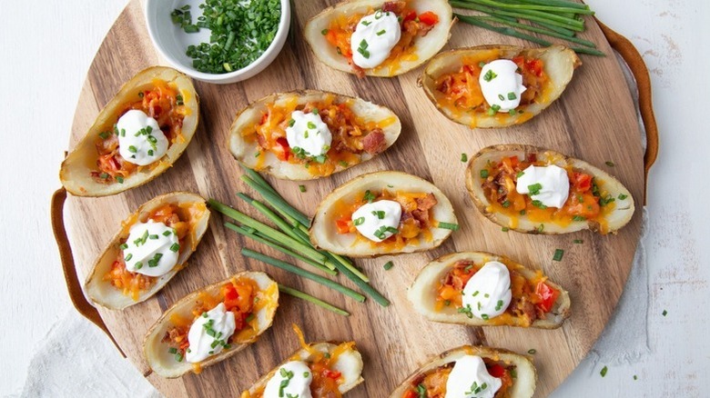 Loaded potato skins on wooden serving board, topped with sour cream and chopped chives