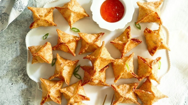 Crab rangoon on white serving plate with small bowl of sweet chili dip