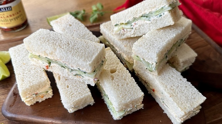 Pile of spicy cucumber tea sandwiches on wooden serving board
