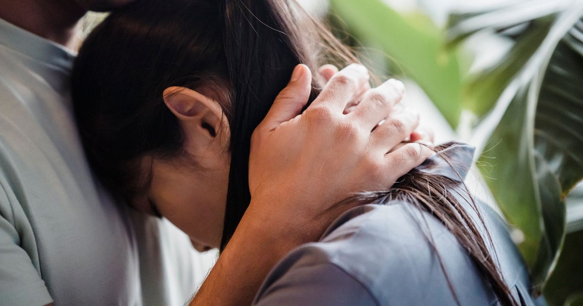 A close-up of a comforting embrace between a man and a woman surrounded by greenery.