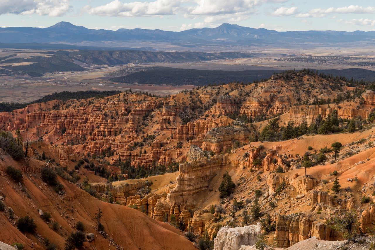 Rocky terrain with ridges and mesas distant flatlands and mountains under a partly cloudy sky