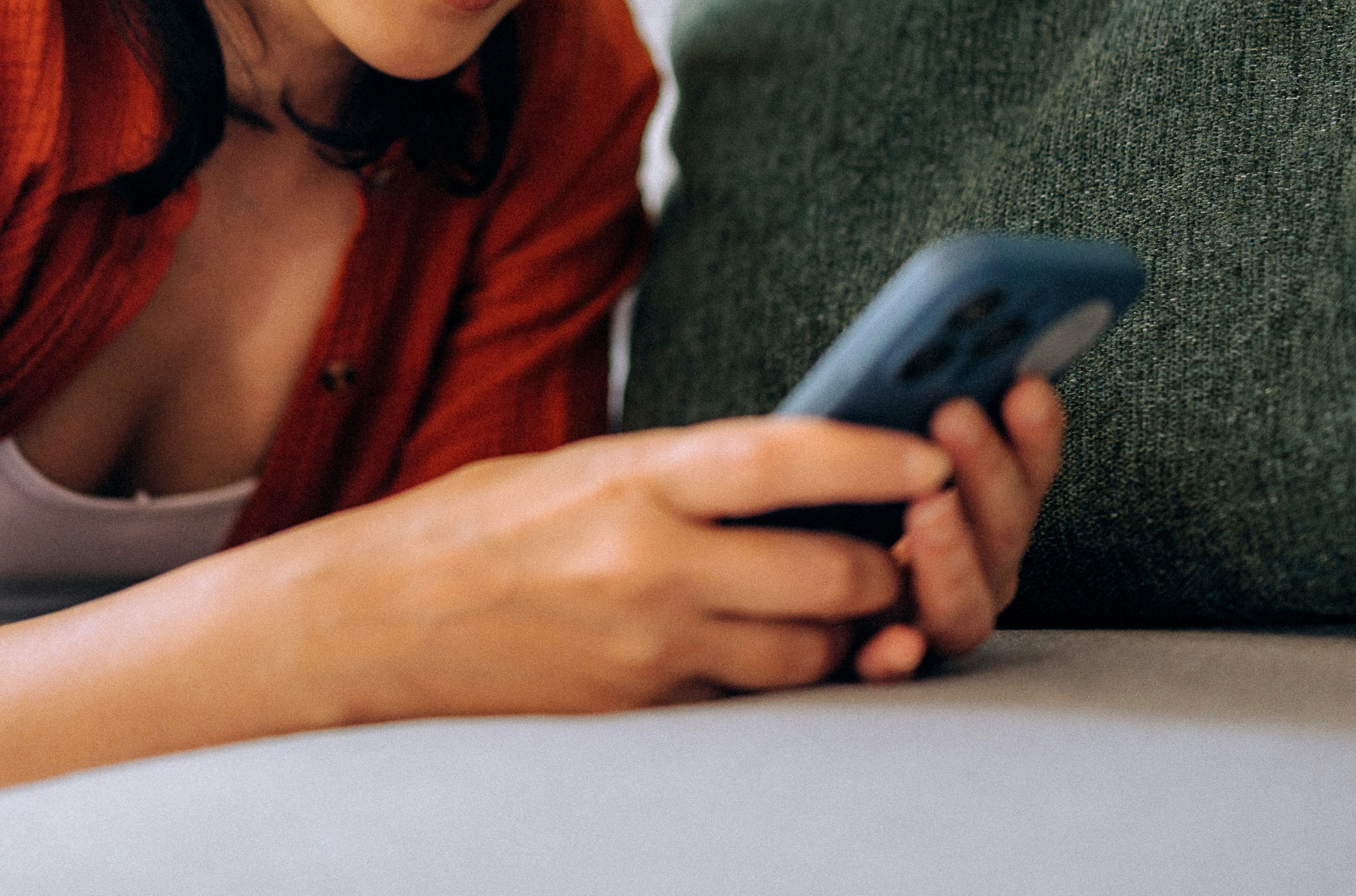Woman lying on couch, smiling at smartphone, wearing casual attire with headphones; conveys relaxed moment related to communication or connection