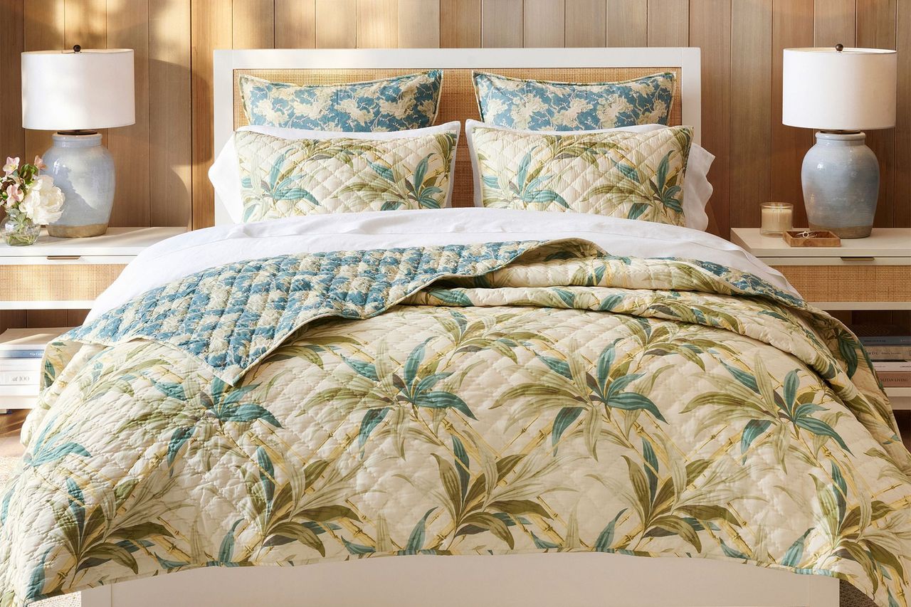 A bed with matching tropical and floral themed quilt and pillows flanked by nightstands with matching lamps and decor