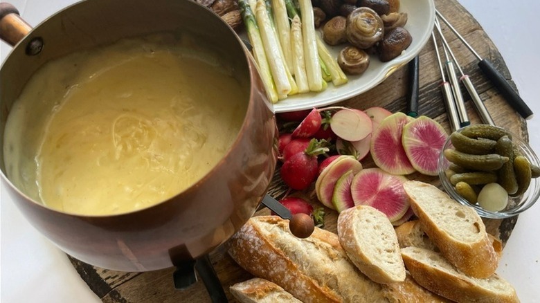 Pot of cheese fondue served with crusty baguette and vegetables