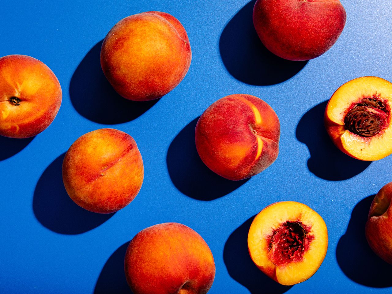 Whole and halved yellow peaches on a blue background