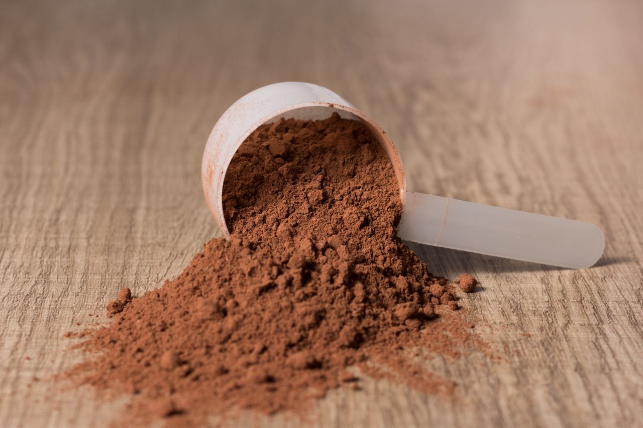 Scoop of brown powder spilled on a wooden surface