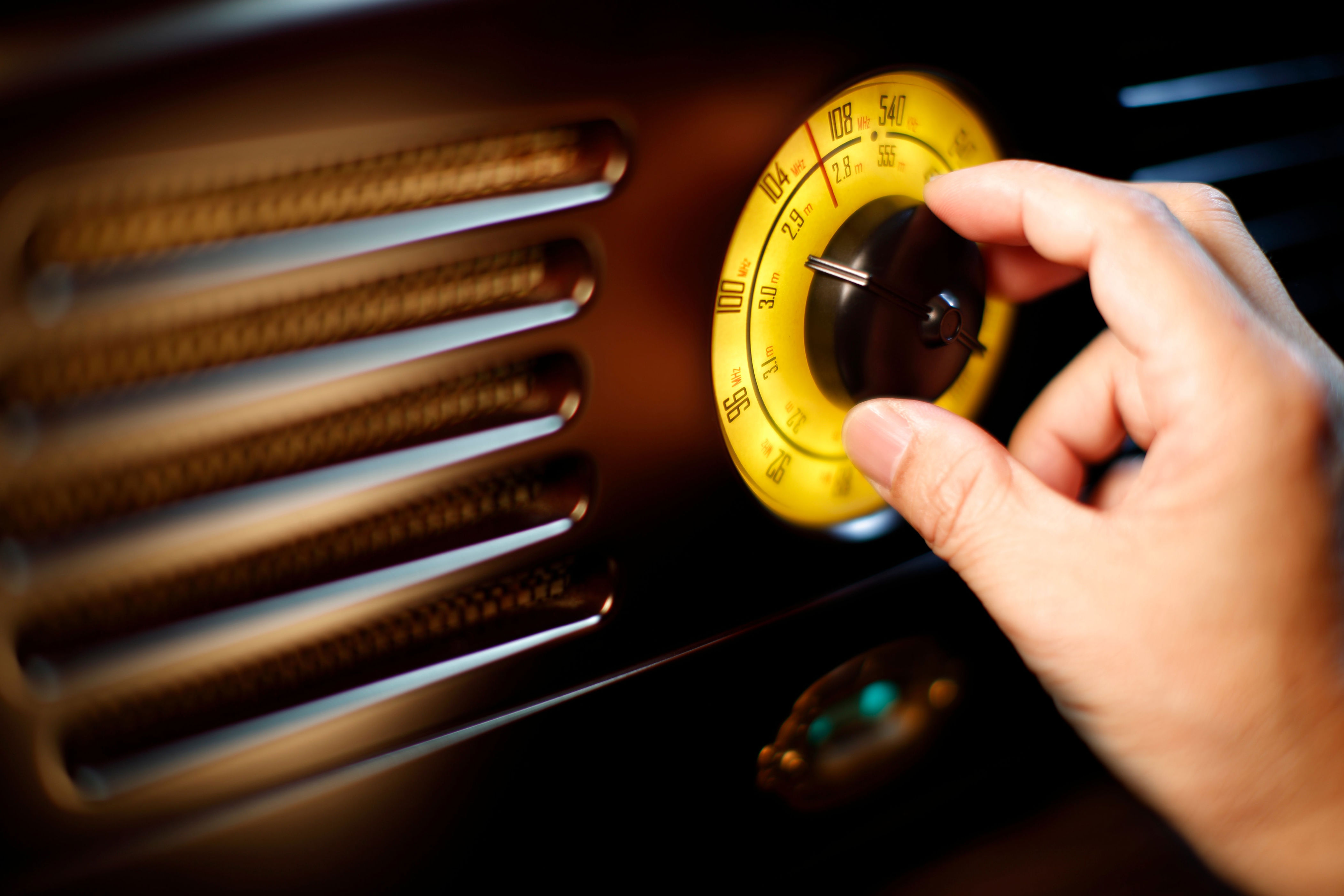 Hand adjusting a vintage radio dial with a decorative yellow faceplate, focusing on tuning