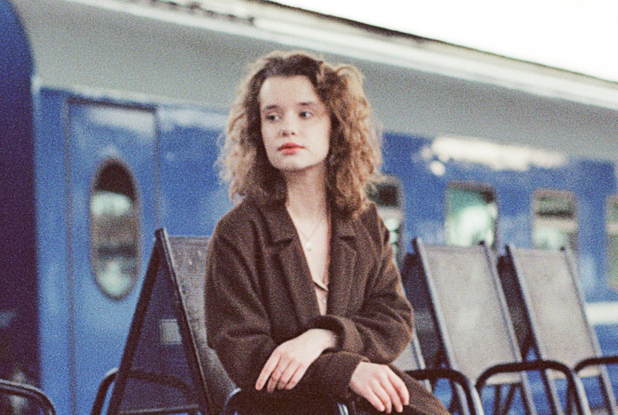 Woman in a coat sits on a bench at a train station, with a train stopped in the background