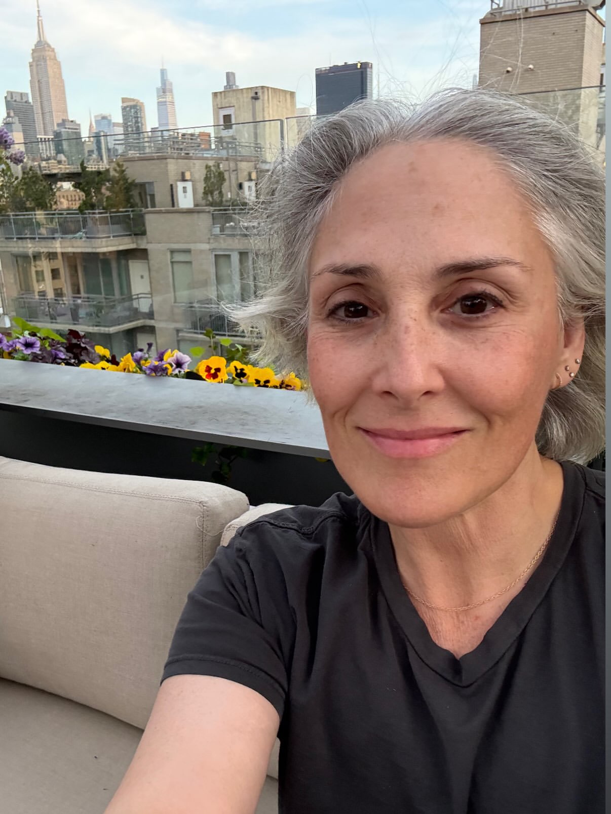 Ricki Lake on her two-year facelift anniversary, smiling in a selfie with a city skyline in the background.