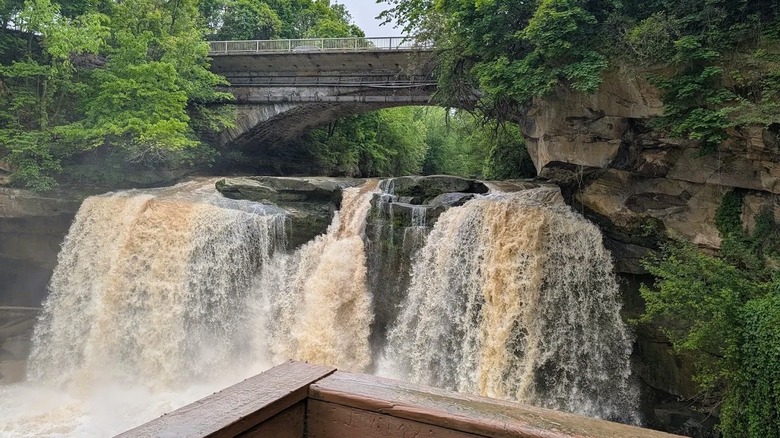 Views from an overlook at Cascade Park in Ohio of a gushing waterfall flowing over sandstone rocks with a bridge above it