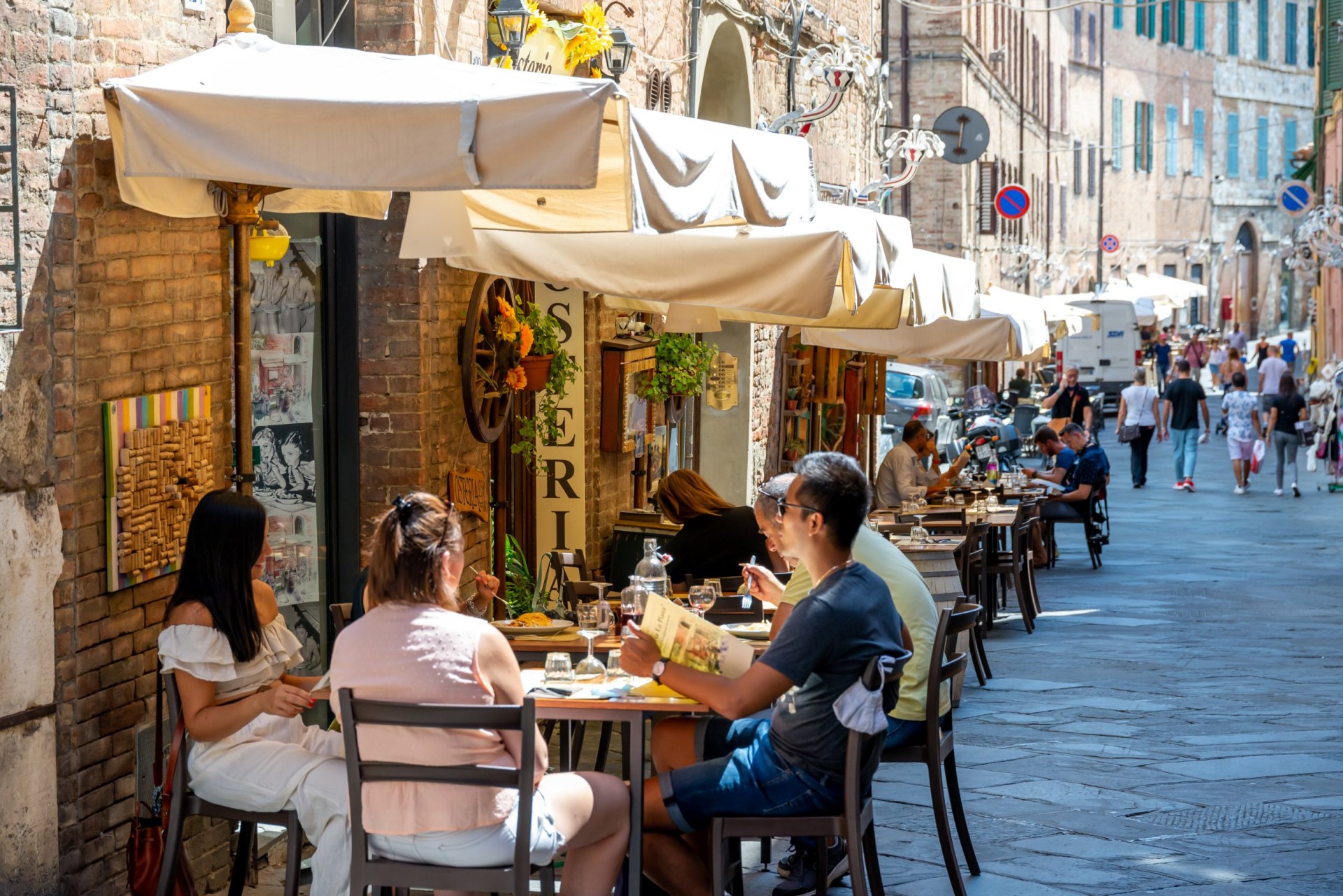 A restaurant in a pedestrian street with small canopies in Italy, where tourists and passers-by eat and walk by.; Shutterstock ID 1966601632; purchase_order: -; job: -; client: -; other: -