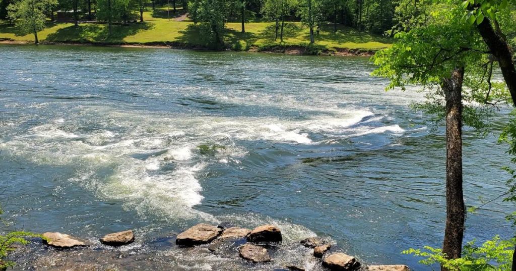 Views of the Ouachita River in Arkansas, with a rocky bed and small rapids, surrounded by lush greenery.