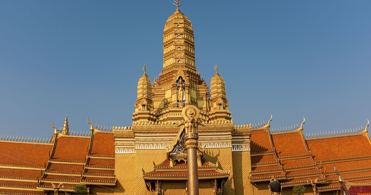 A magnificent golden Buddhist temple in Bangkok against a clear sky, showcasing intricate architecture.