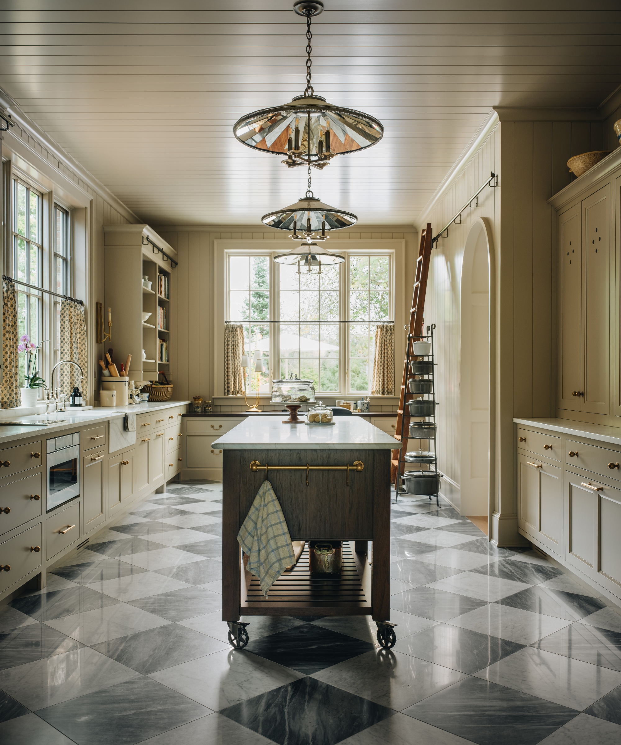 A baker's kitchen with cream walls, a checkerboard floor, and a wooden island on wheels