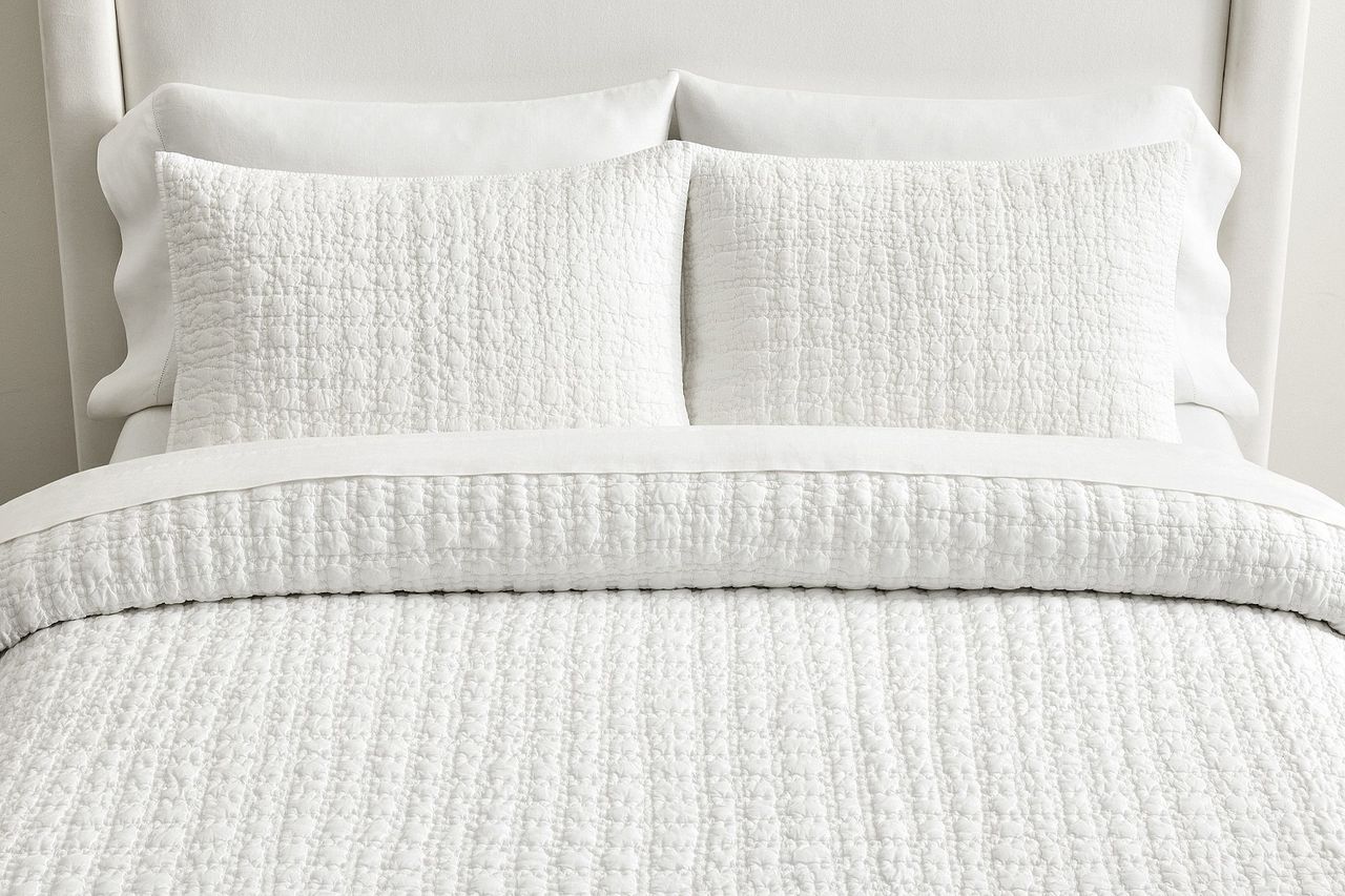 A neatly made bed with a white quilt and matching pillows featuring a textured pattern