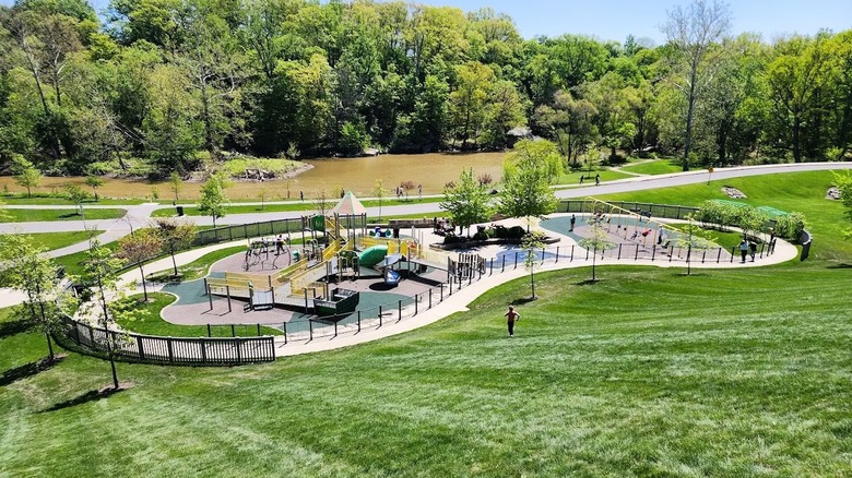 A steep grassy hill leading to a playground at Cascade Park in Ohio, with a flowing river in the background surrounded by trees