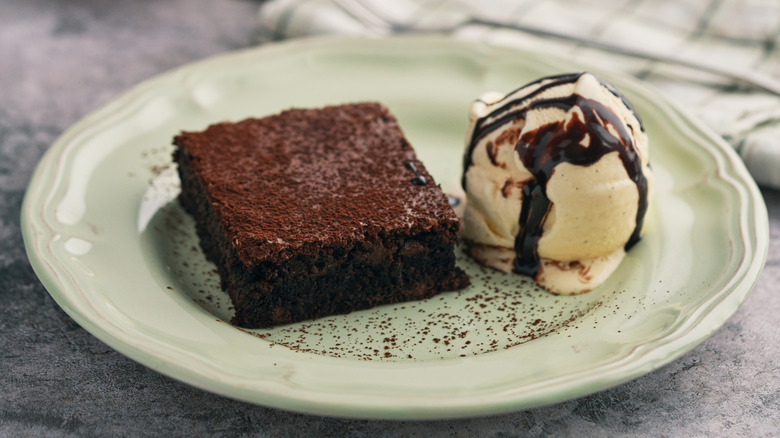 A brownie and alongside a scoop of ice cream with chocolate syrup on a plate