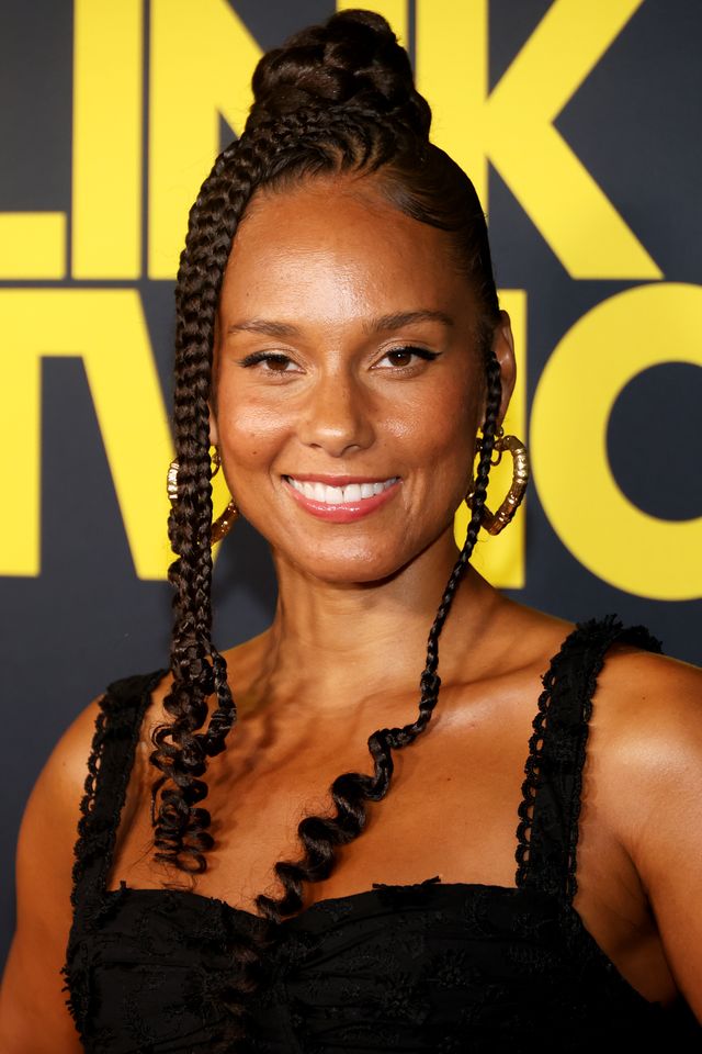 Alicia Keys smiling at an event wearing a braided hairstyle and earrings