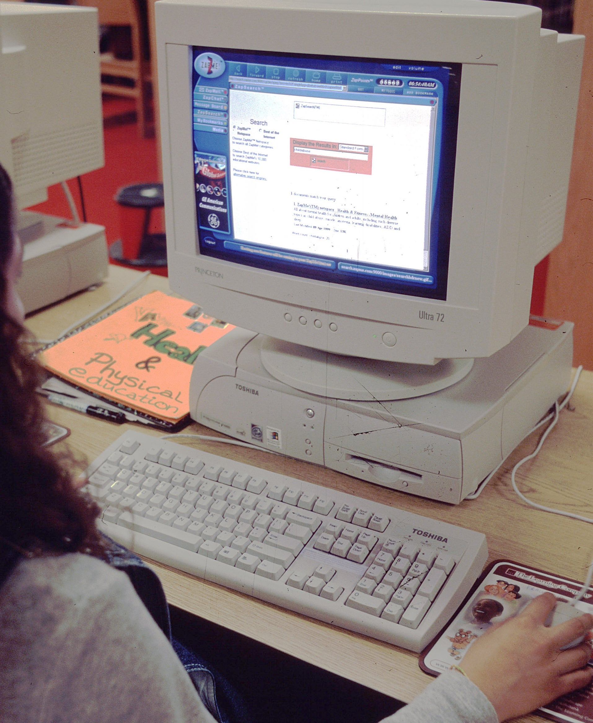 Person using a large desktop computer in a library, focused on the screen displaying a web page