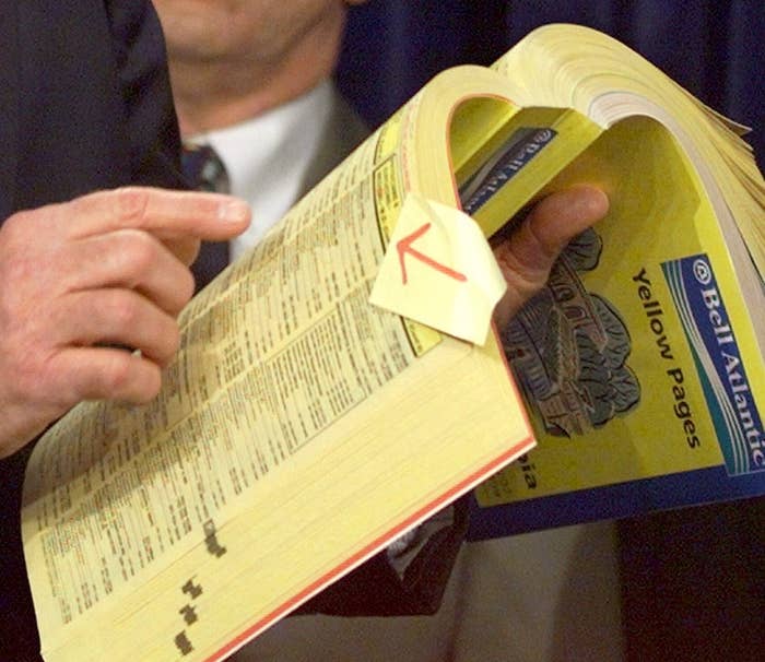 Person flipping through a thick Yellow Pages book, holding it with fingers and using a paper bookmark with a red arrow