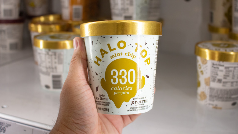 A hand holding a pint of Halo Top ice cream.
