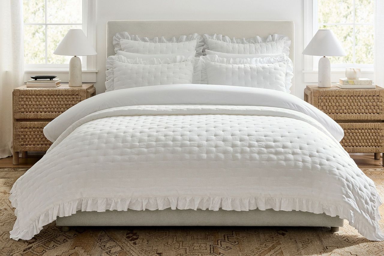 A neatly made bed with tufted bedding and ruffled details flanked by wicker nightstands and table lamps