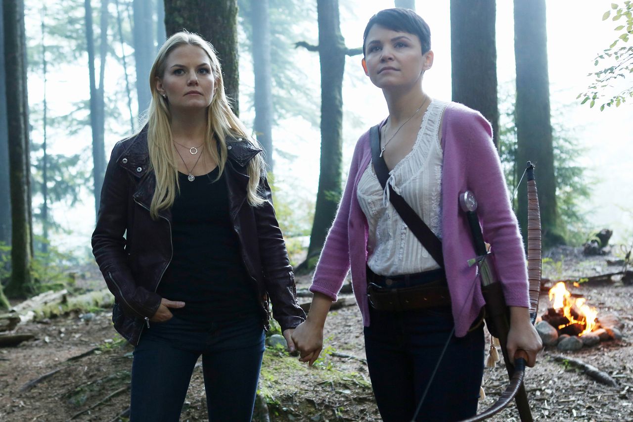Jennifer Morrison and Ginnifer Goodwin standing in a forest holding hands and looking ahead with determination