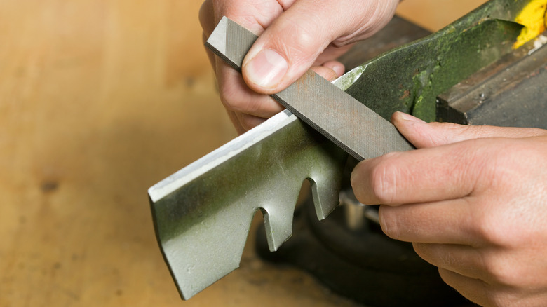 Person using a file to sharpen mower blades