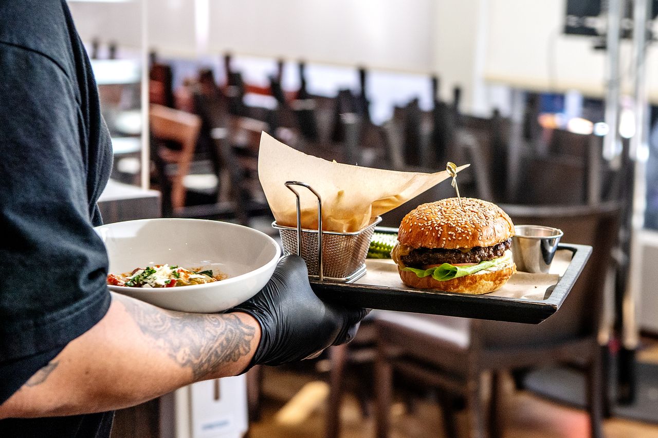A tray with a burger and fries served alongside a bowl of salad carried by a server in a restaurant