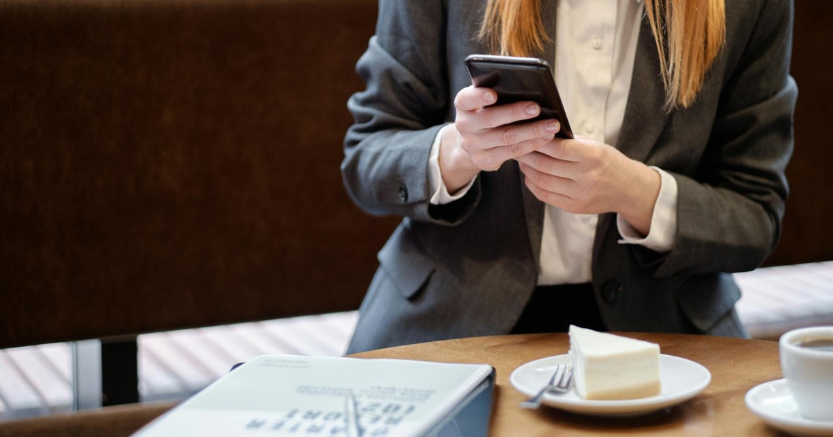 Businesswoman using smartphone in a café, with slice of cake and coffee.