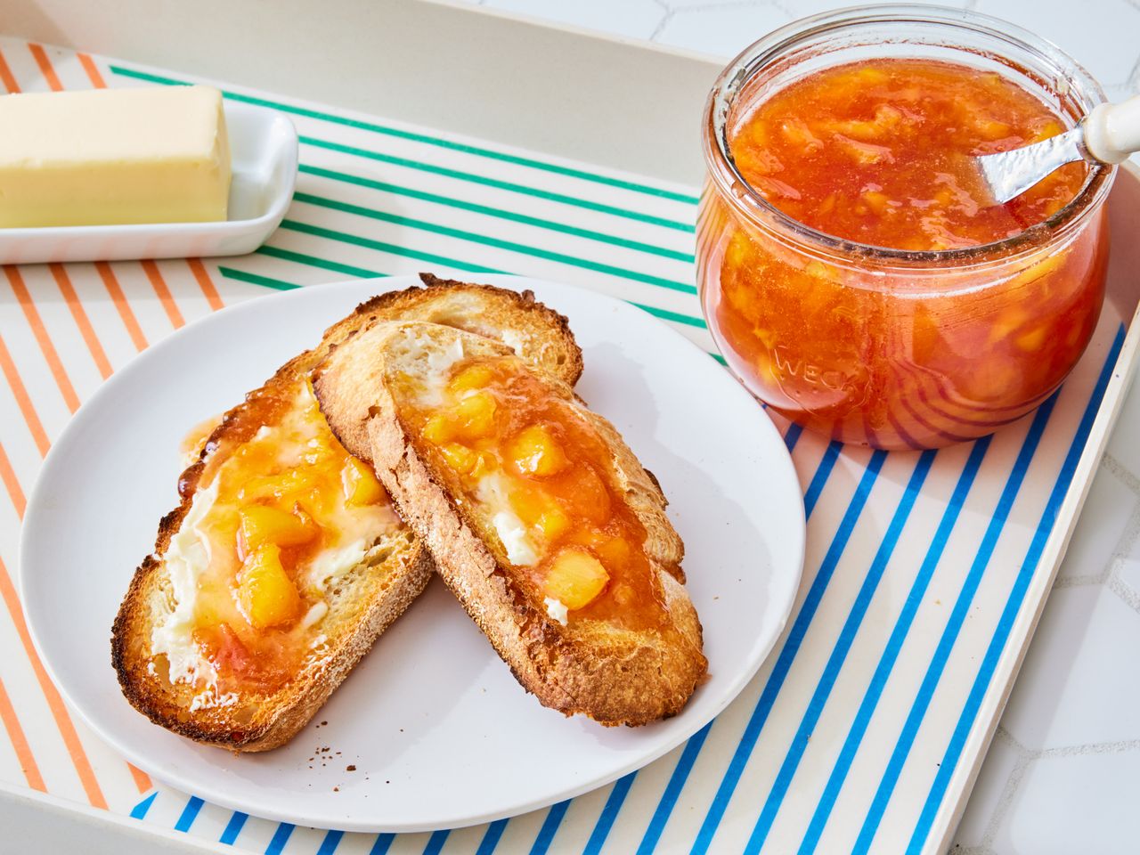 A jar of peach preserves with two slices of toasted bread topped with butter and peach preserves