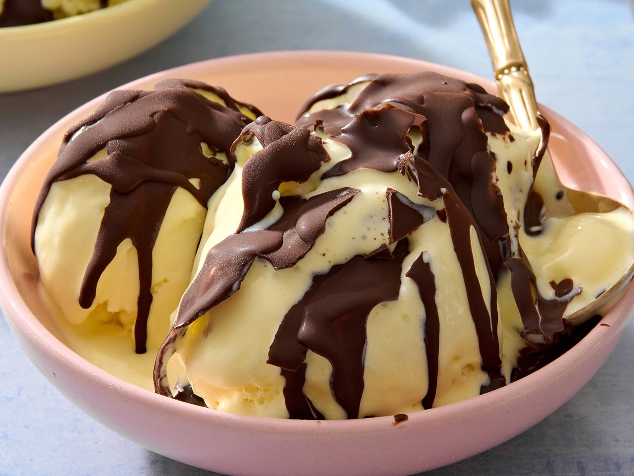 Three scoops of ice cream topped with a chocolate hard shell served in a bowl with a spoon
