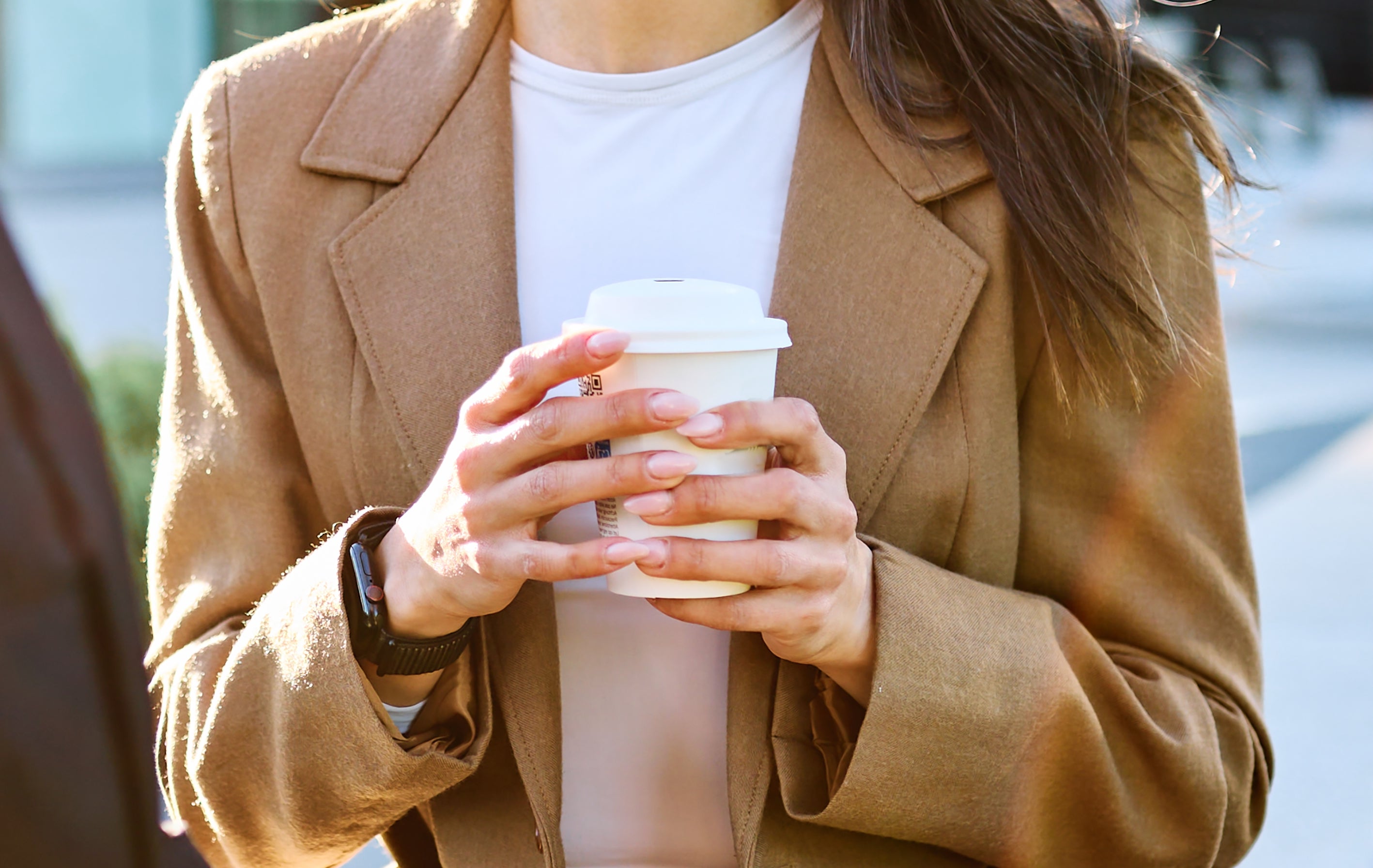 Two people are conversing outdoors. A woman in a blazer holds a coffee cup, looking at the man attentively