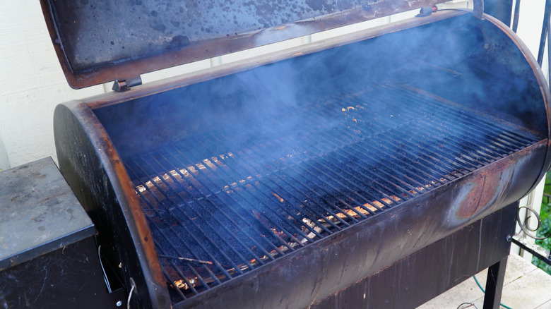 An open Traeger grill preheating, with smoke billowing from the cooking chamber
