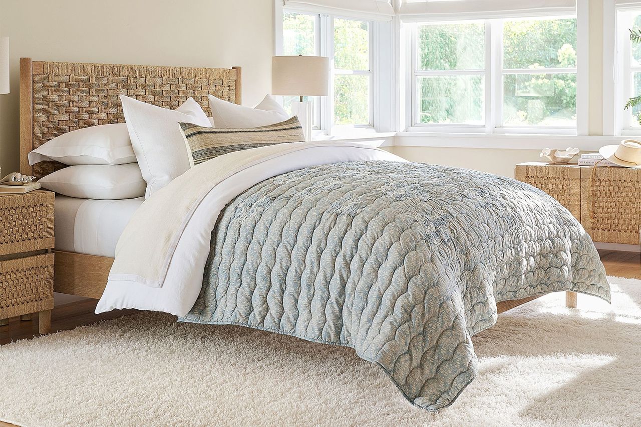 A bedroom with a bed featuring a textured quilt and pillows natural light coming through the windows in the background