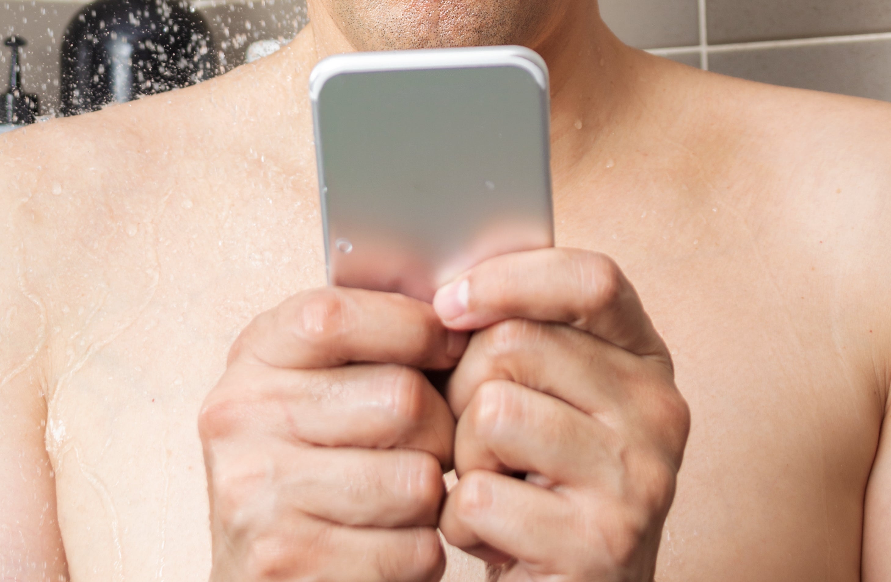 Man in shower using smartphone, water streaming down