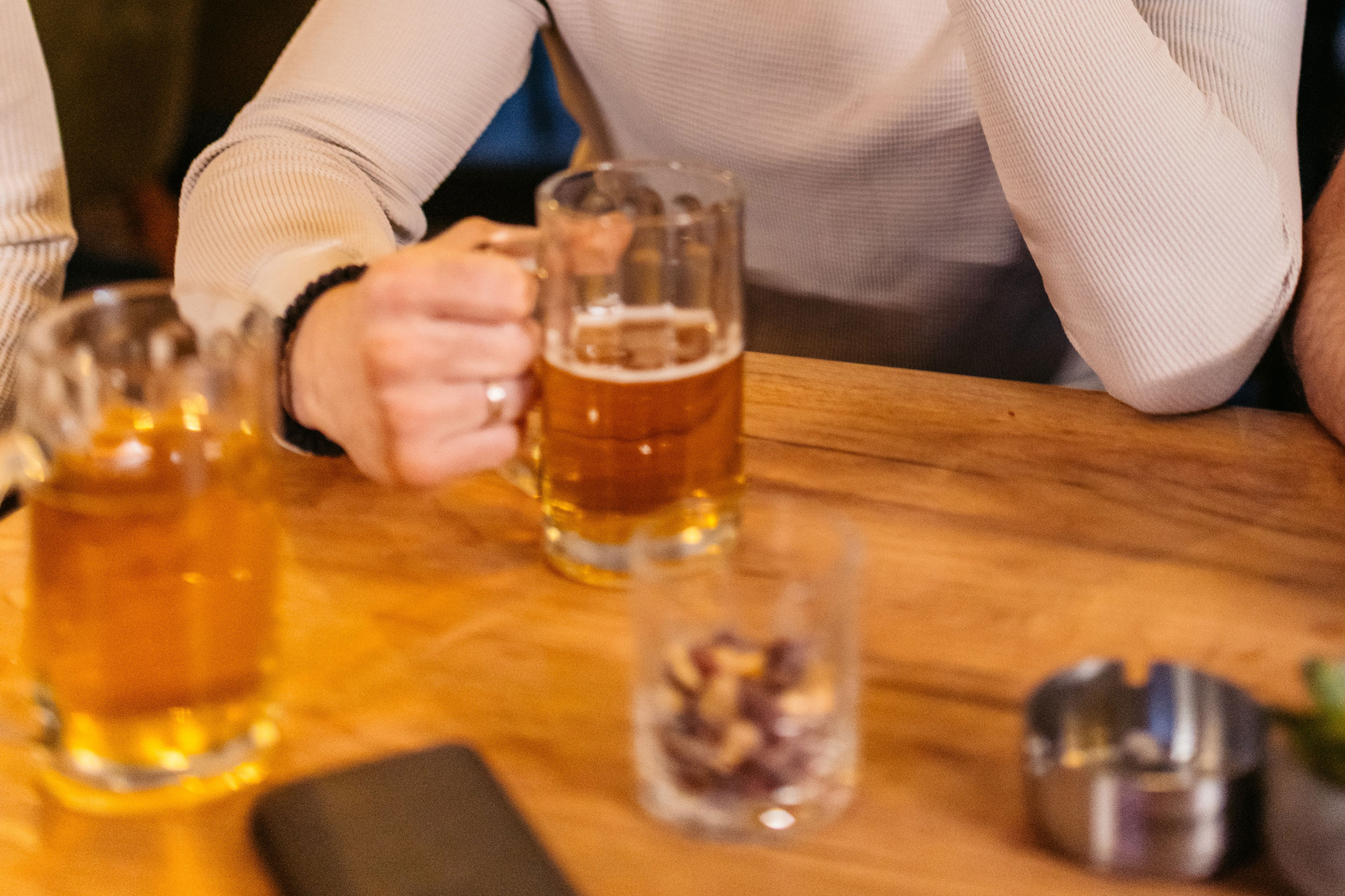 Person at a table with a beer looking tired or contemplative; another person in the background is cheering or celebrating